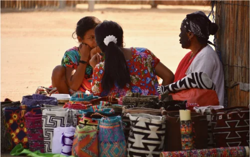 Mujeres wayuu tejiendo y vendiendo mochilas